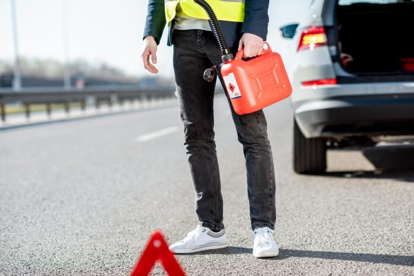 Man with refuel canister on the roadside with his car on the background, close-up view with no face